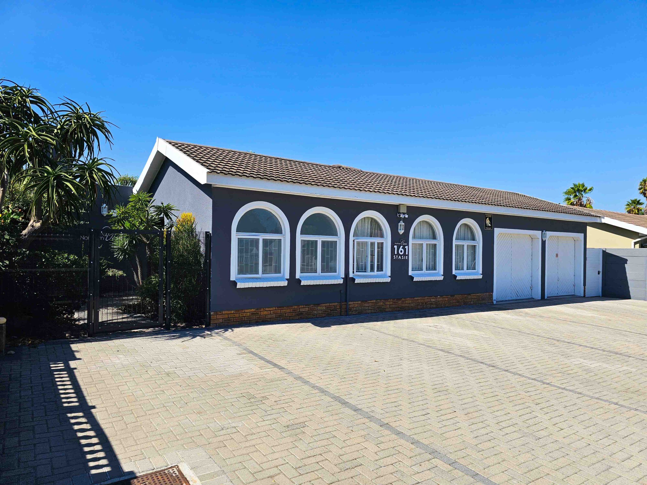 : "Exterior view of Northern Vine B&B in Brackenfell, showcasing a spacious building with arched windows and a large parking area.
